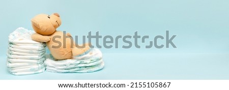 Stack of diapers with cute teddy bear toy lying on table. set for infant newborn boy girl for baby shower present gift on blue background with copy space. Healthcare medical, hygiene concept.
