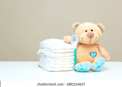 Stack of diapers with toy teddy bear with spoon on table. set for baby shower with copy space