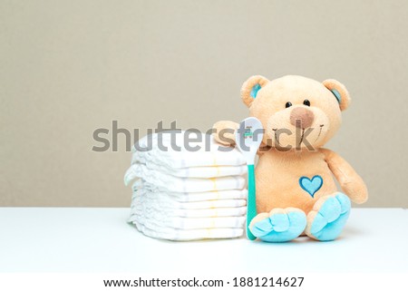 Stack of diapers with toy teddy bear with spoon on table. set for baby shower with copy space