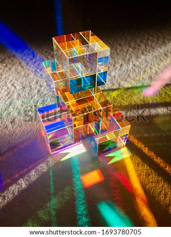 Stack of dichroic coloured glass cube spread ray of artificial light into several spectrum colours. Reflection and refraction of light and lighting. Colourful stripe pattern on texture white paper. 