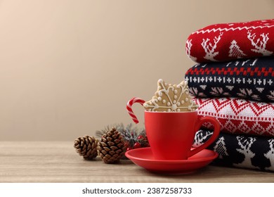 Stack of different Christmas sweaters, cup with candy cane, cookie and festive decor on wooden table, space for text - Powered by Shutterstock