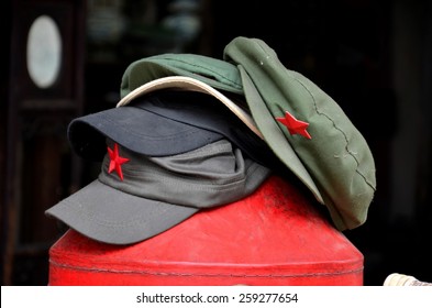 A stack of different colored Mao style communist caps rests on a red holder. The communist red star is prominently displayed in the front of each hat. 