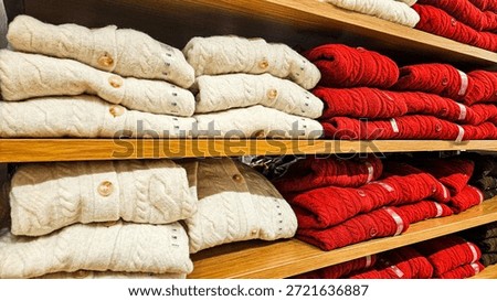 Stack of different colors folded sweaters, red and white knit sweaters in different sizes on a wooden shelf in a clothing store. Shopping concept, insulation for autumn and winter.