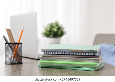 Stack of different notebooks with pencils holder and laptop on wooden desk in classroom