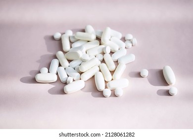 Stack of different pills, heap vitamin capsules on pastel pink background. Dietary supplement supports for health.