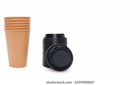 A stack of disposable coffee cups and black plastic lids for them on a white background with free space for text. Cardboard cups made of kraft cardboard, which can be recycled. Disposable paper cups.