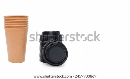 A stack of disposable coffee cups and black plastic lids for them on a white background with free space for text. Cardboard cups made of kraft cardboard, which can be recycled. Disposable paper cups.