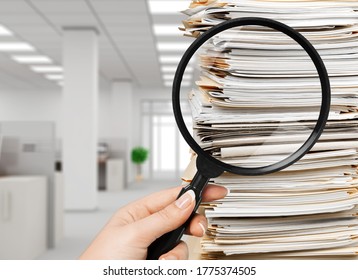 Stack of document papers and hand with a magnifying glass