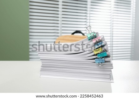 Stack of documents attached with colorful binder clips on white table in office