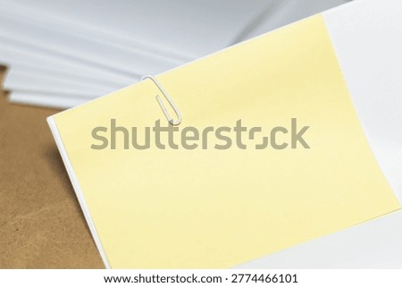 A stack of documents held together with a paperclip and a blank yellow sticky note; a minimalist composition depicting administrative organization without human intervention