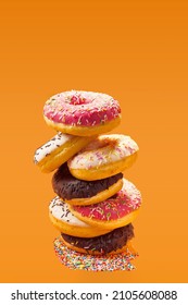 Stack of donuts on orange background including chocolate frosting, topping, coconut and frosting
