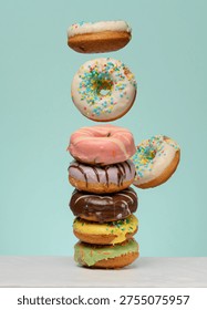 Stack of donuts with various fillings and glazes, several levitating upwards. Blue background.