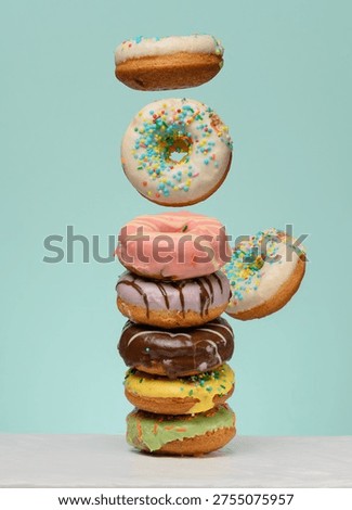 Stack of donuts with various fillings and glazes, several levitating upwards. Blue background.