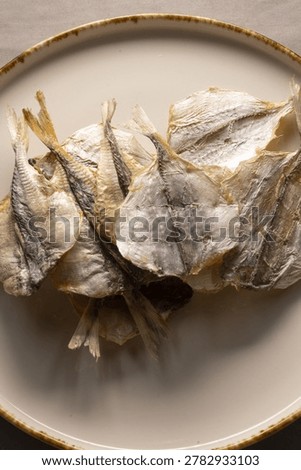 Stack of dried fish on plate, arranged preserved catch ready for longterm storage or cooking, neutral porcelain and linen setting,