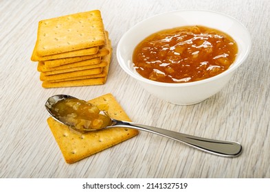 Stack of dry cookies, bowl with lemon jam, teaspoon with jam on cracker on wooden table