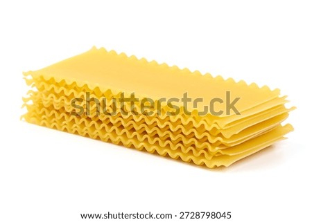 Stack of dry lasagna pasta sheets with ruffled edges, light yellow color, culinary ingredient, isolated on white background