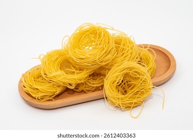 Stack of dry pasta nests on wooden plate, isolated on white background