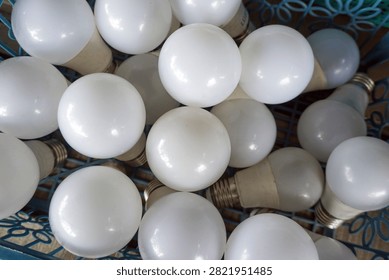 A stack of dull white round LED light bulbs in a basket. Industrial patterns highlight themes of energy efficiency, waste management, or electrical hardware.