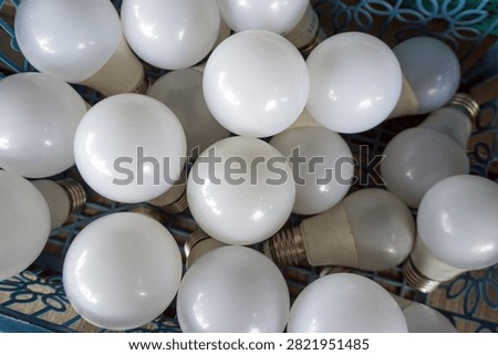 A stack of dull white round LED light bulbs in a basket. Industrial patterns highlight themes of energy efficiency, waste management, or electrical hardware.