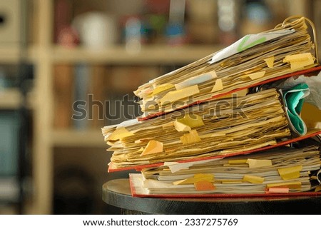 stack of dusty messy file folders with narrow depth of field, blurred office in the back,red tape, bureaucracy,aministration,business concept. 