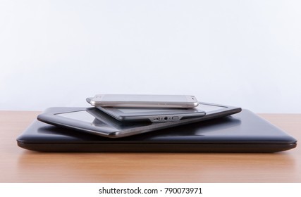 Stack Of Electronic Gadgets On A Table - Notebook, Tablet, Ebook Reader And A Smatphone On The Top