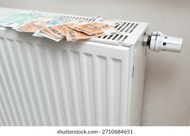 A stack of euro banknotes placed on a white radiator, symbolizing warmth and financial stability in a cozy indoor setting. Ideal for themes of finance and home comfort.