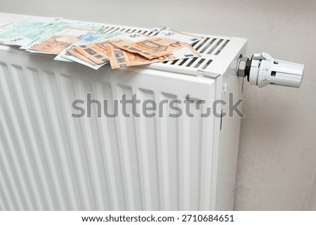 A stack of euro banknotes placed on a white radiator, symbolizing warmth and financial stability in a cozy indoor setting. Ideal for themes of finance and home comfort.