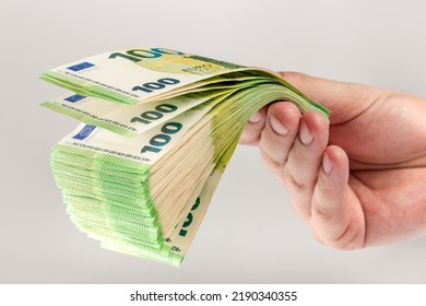 Stack Of Euro Bills In Hand. A Large Stack Of 100 Euro Banknotes In A Male Hand On A Uniform Gray Background. The Concept Of Financial Assistance, Real Estate Purchase, Loan Or Insurance Payment.