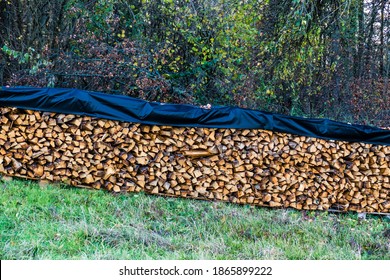 Stack of firewood covered with a flat, weatherproof cover on meadow
