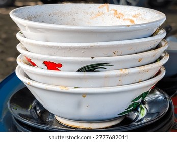 A stack of five dirty, empty white ceramic bowls with traditional rooster illustrations on a table after a meal, representing street food culture and dining.