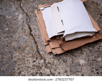 Stack of flattened cardboard sheets prepared for recycling on concrete ground outdoors. Brown paper packaging waste with sustainability and eco waste management concept.