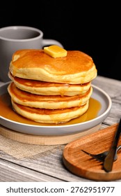 Stack of fluffly pancakes with butter and syrup on a plate, rustic background