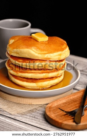 Stack of fluffly pancakes with butter and syrup on a plate, rustic background