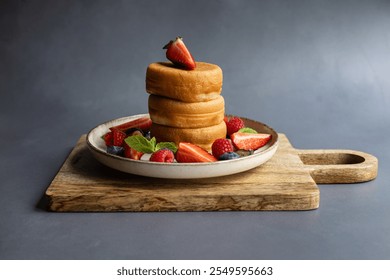 Stack of fluffy Japanese pancakes served with fresh strawberries, raspberries, blueberries, and mint leaves on a rustic wooden board and ceramic plate. Gourmet breakfast, brunch and comfort food - Powered by Shutterstock