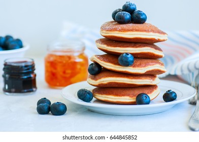 Stack of fluffy panckes with fresh berries, blueberry and orange jam served on a white plate. Healthy breakfast concept.