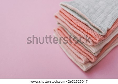 Stack of folded baby socks in soft pastel shades of white, pink, peach, and grey, placed neatly on a pink background. Cozy and minimal flat lay composition.