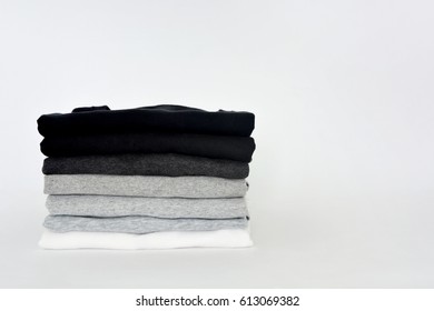 stack of folded black, grey and white color (monochrome) t-shirt on white background, copy space