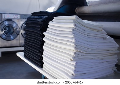 Stack Of Folded Black And White Cloths In An Industrial Laundry.  Cleaning Service For Hospitals And Hotels.