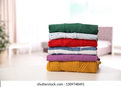 Stack Of Folded Bright Clothes On Table Against Blurred Background. Space For Text