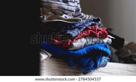 Stack of Folded Colorful Clothes Placed on Bed in Home Interior with Soft Natural Light Coming from Window
