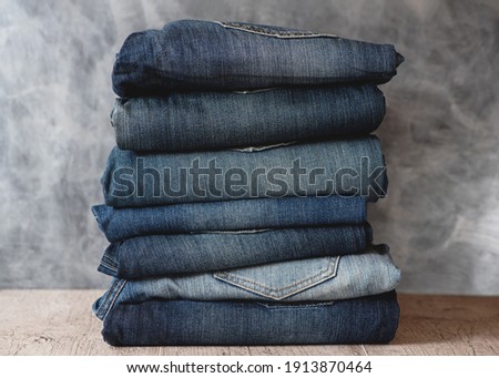 Stack of folded jeans on shelf against gray wall. Closeup of denim in different colors