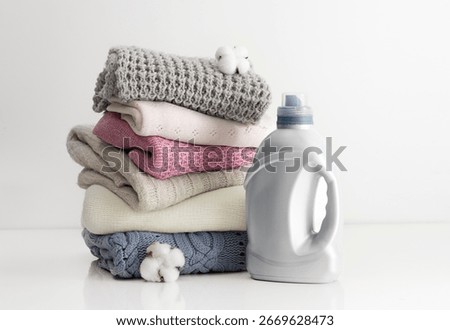 Stack of folded knitted clothes and washing gel,softener on table .Household apparel.Woolen sweaters stacked.Objects.
