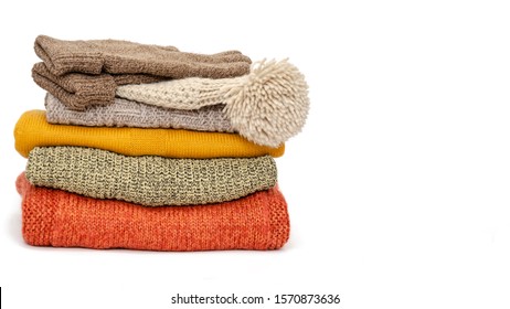 A stack of folded knitted warm women sweaters, hat and gloves on a white background. Season of warm clothes. Copy space