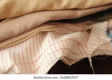 Stack of folded linen fabric in a sewing atelier. Soft colors canvas, textured textile, woven linen fabric. Aesthetic textile collection in a dressmaker workshop. 