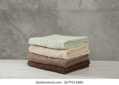 Stack of folded towels on light wooden table against grey wall
