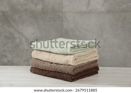 Stack of folded towels on light wooden table against grey wall