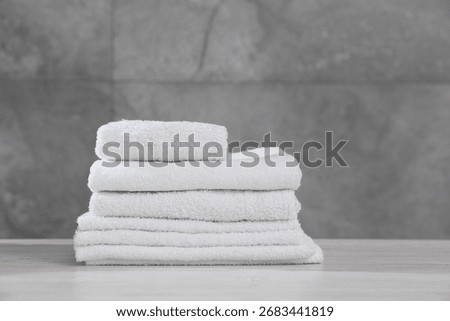 Stack of folded towels on light wooden table against grey wall, closeup