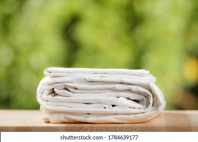 A stack folded white bedding  Bed sheet set blurred foliage background 