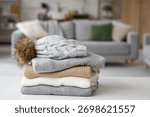Stack of folded winter clothes with hat on table in room, closeup