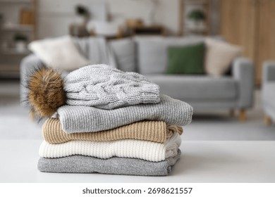 Stack of folded winter clothes with hat on table in room, closeup